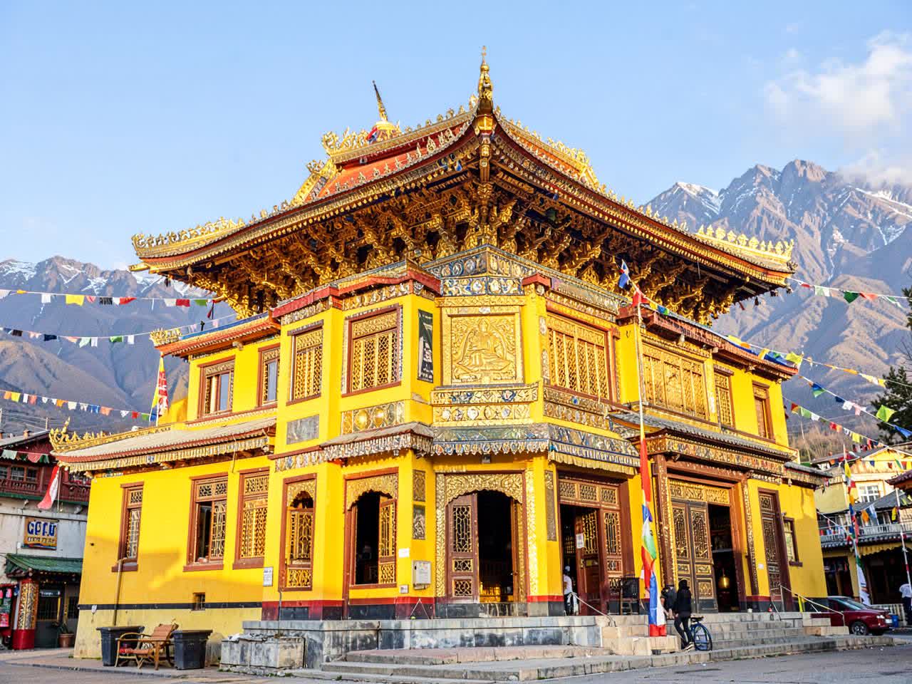 Bright yellow and gold Gyuto monastery with prayer flags and mountains behind
